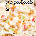 Overhead view of a creamy taffy apple salad in a white bowl, filled with chunks of red and green apples, mini marshmallows, chopped peanuts, and drizzled caramel. Surrounding the main bowl are smaller dishes with more ingredients and a spoonful of salad in the foreground. Bold text overlay reads “Taffy Apple Salad” and “Easy to Make Holiday Recipe.”