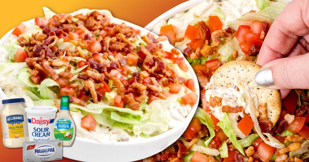 Overloaded BLT dip in a white serving bowl with a creamy ranch and cream cheese base, topped with shredded lettuce, diced tomatoes, and crispy bacon, with a hand dipping a cracker into the thick, scoopable dip for a party appetizer.
