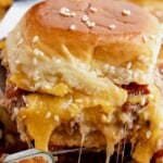 Tall stack of bacon cheeseburger sliders made with ground beef, crispy bacon, and melted cheddar on soft sesame slider buns, with gooey cheese stretching as one slider is lifted.