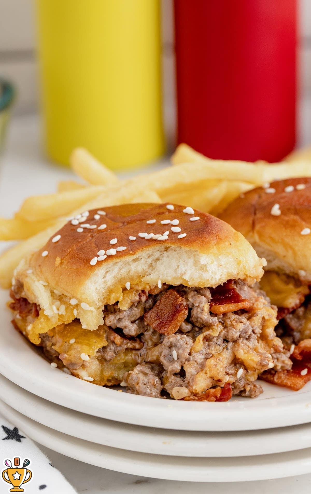 Close-up of a bacon cheeseburger slider with juicy ground beef, crispy bacon, and melted cheese on a soft sesame bun, with cheese pulling as it&rsquo;s lifted.
