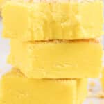 Tall stack of creamy banana fudge squares with a smooth yellow center and vanilla wafer crumb topping, featuring text overlay highlighting a vintage no-bake banana fudge recipe.