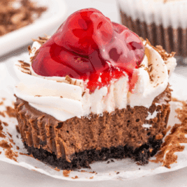 Black Forest mini cheesecake topped with whipped cream and cherry filling, with a bite taken out.