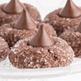 Chocolate kiss cookies rolled in sugar and topped with a Hershey’s Kiss on a glass plate.