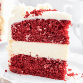 Slice of red velvet cheesecake with cream cheese frosting and layered red velvet cake.