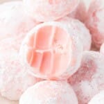 Homemade strawberry truffles rolled in powdered sugar with a creamy pink center, shown alongside fresh strawberries and ingredient measurements for the recipe.