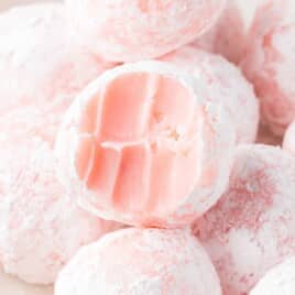 Homemade strawberry truffles rolled in powdered sugar with a creamy pink center, shown alongside fresh strawberries and ingredient measurements for the recipe.