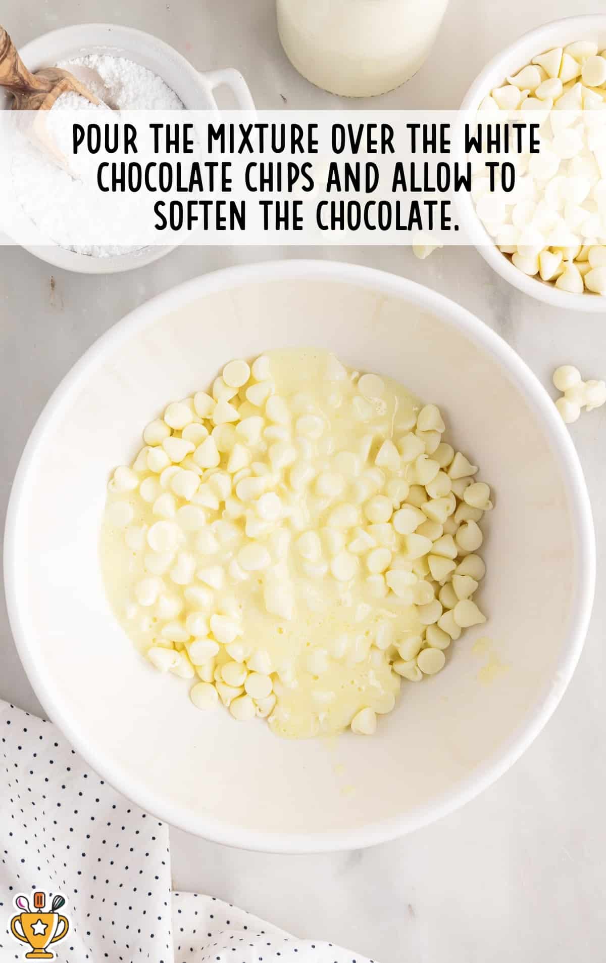 Warm cream and butter mixture poured over white chocolate chips in a large white bowl, beginning to soften the chocolate as it melts around the edges.