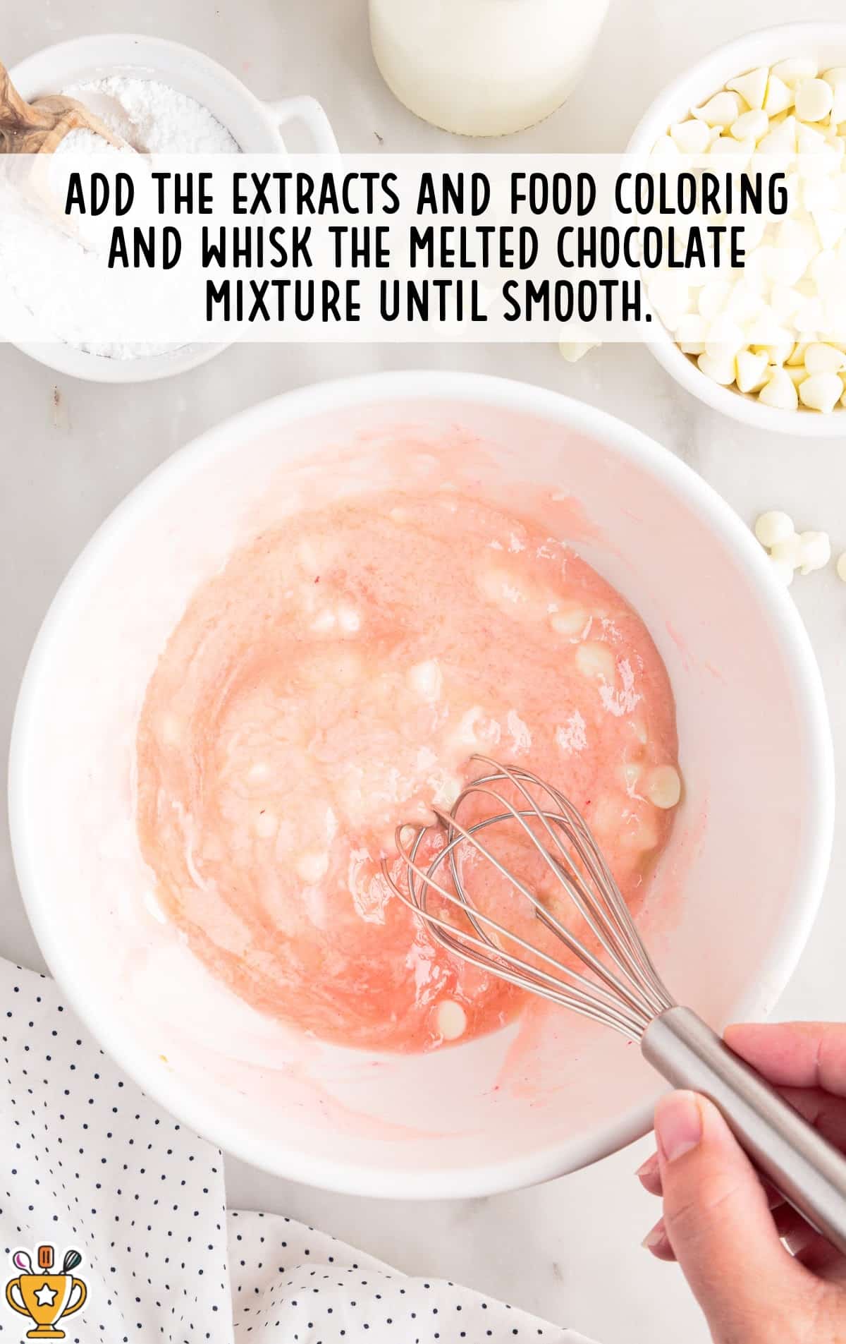 Strawberry truffle mixture being whisked in a white bowl, turning pale pink as strawberry extract and food coloring are blended into the melted white chocolate until smooth.