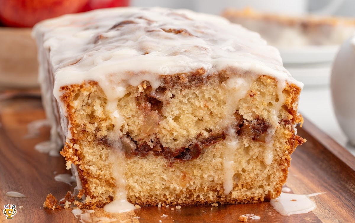Vertical hero image of apple fritter bread slices with heavy glaze dripping over the edges, highlighting the cinnamon apple swirl inside, with bold text reading “Bakery-Style Apple Fritter Bread Recipe” and “With Homemade Glaze!” alongside a small apple icon.