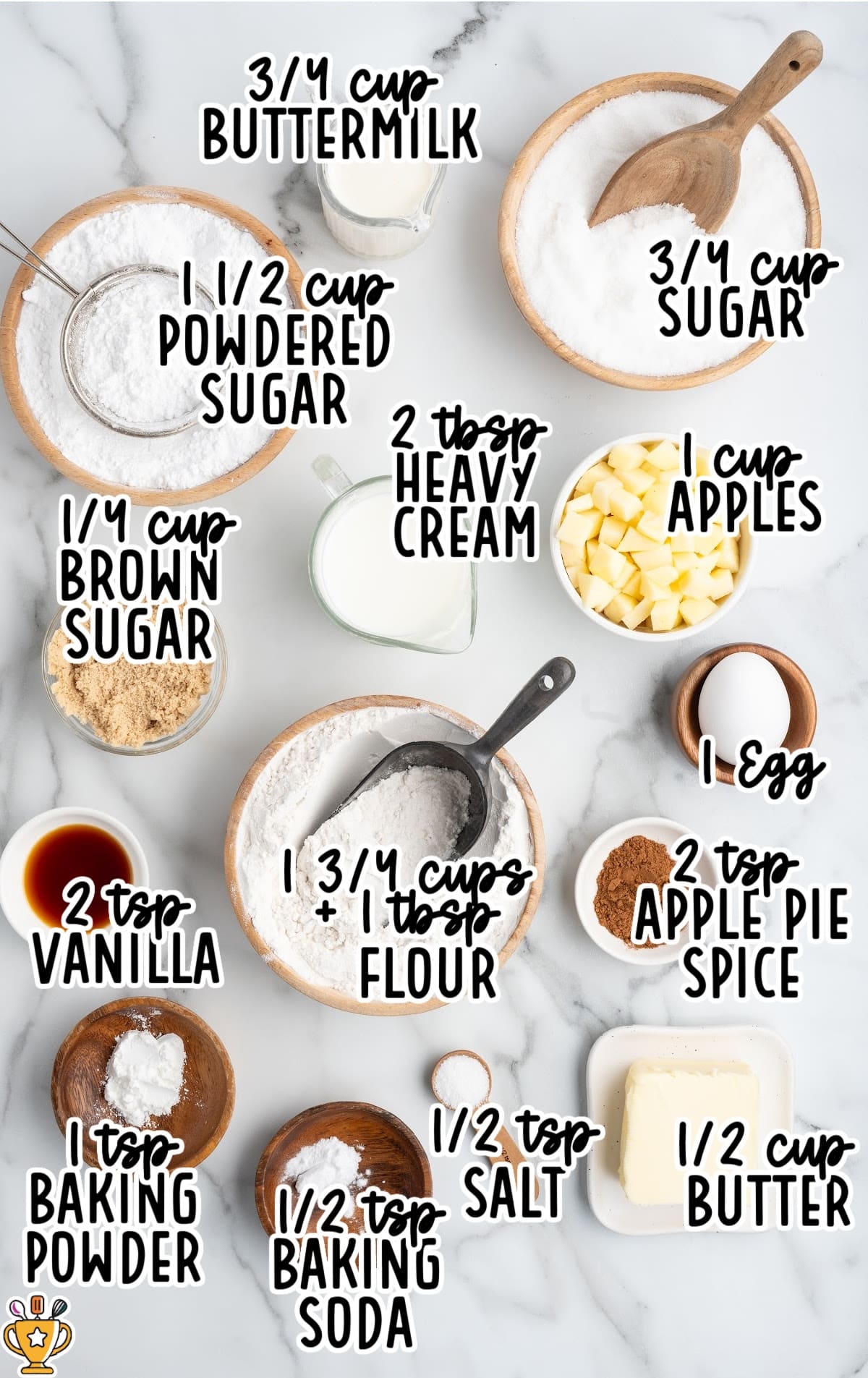 Overhead flat lay of apple fritter bread ingredients arranged in bowls on a white marble surface, labeled with text showing measurements for flour, butter, sugar, brown sugar, apples, buttermilk, vanilla, egg, baking powder, baking soda, salt, apple pie spice, powdered sugar, and heavy cream.
