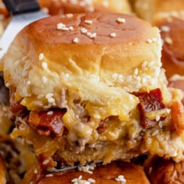 Warm bacon cheeseburger slider topped with melted cheese and sesame buns.