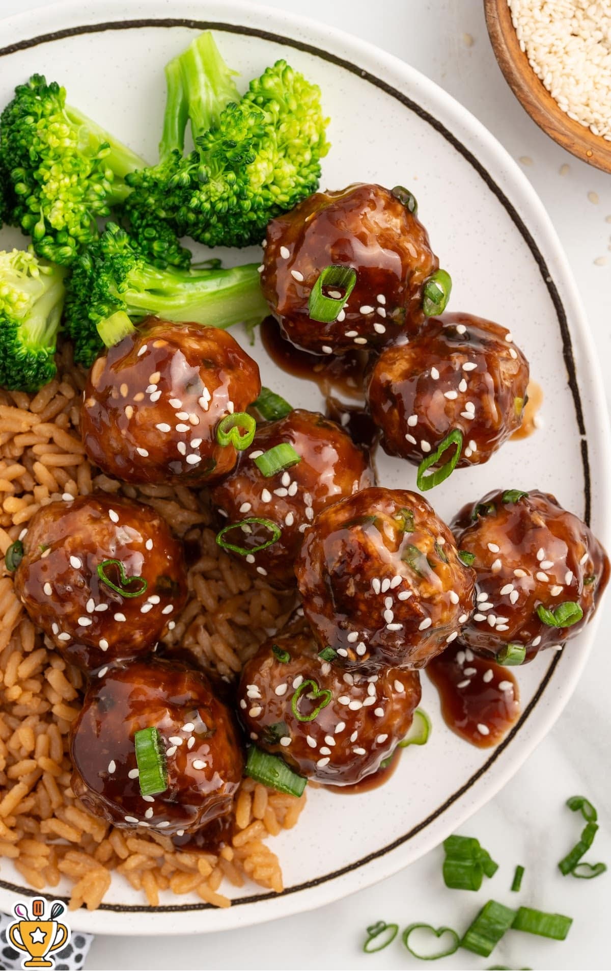 Overhead view of Asian turkey meatballs coated in a glossy sauce on a plate with rice and broccoli, finished with sesame seeds and sliced green onions.