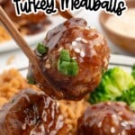 Asian turkey meatballs coated in a glossy soy-hoisin glaze, lifted with chopsticks and sprinkled with sesame seeds and green onions, served with rice and broccoli for an easy family dinner.