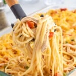 Close-up of creamy chicken spaghetti with shredded chicken and diced peppers lifted from the cheesy baked casserole.