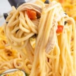Close-up of creamy baked chicken spaghetti with shredded chicken and diced peppers lifted from the casserole, with a small inset image of the baked pasta dish.