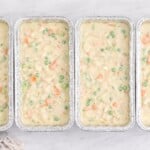 Row of unbaked freezer chicken pot pies filled with creamy chicken and vegetables in foil loaf pans on a white marble surface.