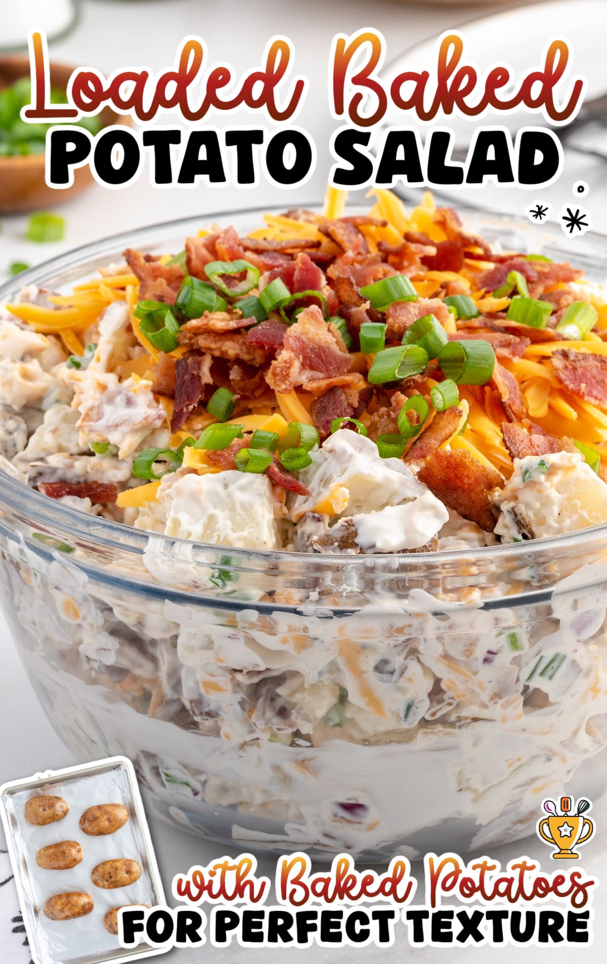 Loaded baked potato salad in a glass bowl with creamy potatoes, crispy bacon, shredded cheddar cheese, and sliced green onions, made with baked potatoes for a fluffy texture.