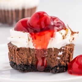 Finished black forest mini cheesecake with whipped topping, cherry pie filling, and chocolate shavings, presented as a recipe card image highlighting the layered chocolate cheesecake and crust.