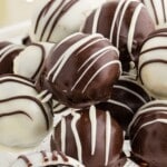 Stacked chocolate and white chocolate Oreo Balls on a white cake stand, drizzled with contrasting chocolate. One Oreo ball is cut open to show the dense Oreo cookie center. Text on the image reads “5-ingredient OREO BALLS for valentines” and “Sweet Bite-size Treat!”