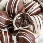 Close-up of Oreo balls coated in milk and white chocolate, with one Oreo ball cut open to show the dense, creamy Oreo and cream cheese filling inside.