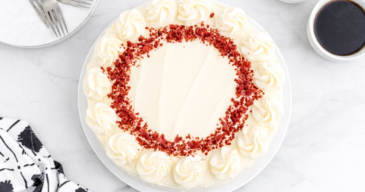 Overhead view of a red velvet cheesecake, decorated with frosting swirls and red velvet cake crumbles.