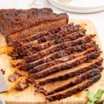 Recipe card image showing sliced slow-cooked brisket on a cutting board with two foil pans of cooked brisket below. Text on the image reads “Slow Cooking Brisket in Oven” followed by ingredient text: “4–5 lb beef brisket, 2 tbsp brown sugar, 1 1/2 tbsp smoked paprika, 1 tbsp chili powder, 1 tbsp garlic powder, 1 tbsp onion powder, 1/2 tsp dry mustard powder, 1/2 tsp cumin, 1 tbsp kosher salt, 1/2 tsp black pepper,” and “Find more recipes at thebestblogrecipes.com.”