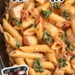 Close-up of creamy tuscan chicken pasta in a dark skillet with penne, chicken pieces, spinach, and sun-dried tomatoes; text reads “The Easiest TUSCAN Chicken Pasta” and “WITH SAVORY sundried tomatoes!” with an arrow pointing to a jar of Alessi sun dried tomatoes.