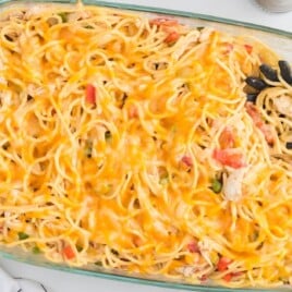 Overhead view of baked chicken spaghetti in a glass casserole dish with melted Colby jack cheese and a serving spoon in the pan.
