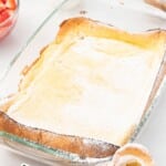 Pinterest graphic of a powdered sugar&ndash;dusted dutch baby baked in a glass dish on a white counter with a coffee cup and fruit nearby; text on image reads &ldquo;DUTCH BABY in just 30 minutes!&rdquo; and &ldquo;so delicious with FRESH FRUIT!&rdquo; with Best Blog Recipes branding.