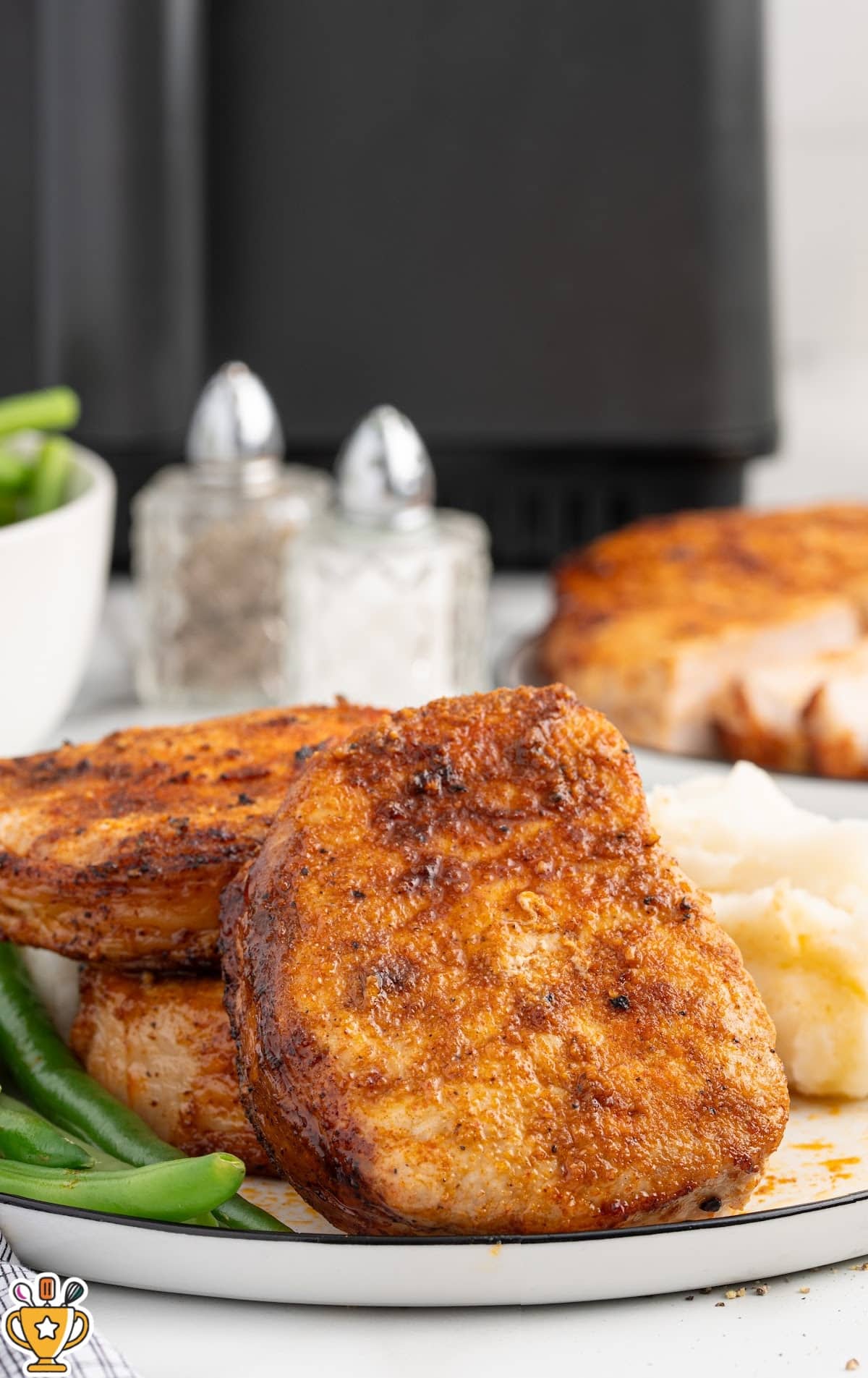 Boneless pork chops in air fryer served on a white plate with creamy mashed potatoes and fresh green beans, highlighting the browned exterior and tender texture of the pork.
