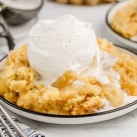 Bowl of Pineapple Dump Cake topped with a scoop of vanilla ice cream, highlighting the soft pineapple filling and buttery crumble topping on a white plate with a fork and napkin in the background.