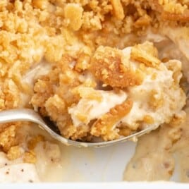 Close-up of a spoon lifting a creamy bite of Ritz Cracker Chicken Casserole from a white baking dish, showing chunks of chicken in a thick sauce and a golden crushed Ritz cracker topping.