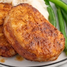 Close-up of golden brown boneless pork chops in air fryer basket, showing a caramelized, seasoned crust with visible spices and juices on the surface for a juicy, perfectly cooked finish.