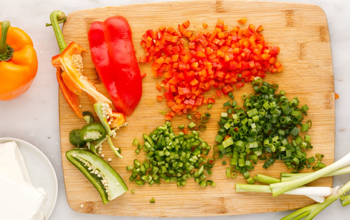 Finely chopped red bell pepper, green onions, and diced jalapeño on a cutting board, prepped for mixing into cream cheese ranch roll ups.