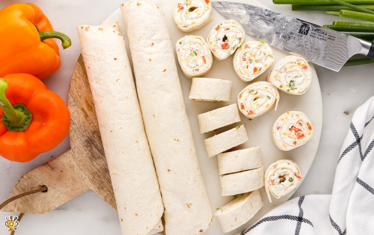 Ranch roll ups rolled into tight tortilla logs and sliced into clean pinwheels on a cutting board, showing even filling and neat edges.