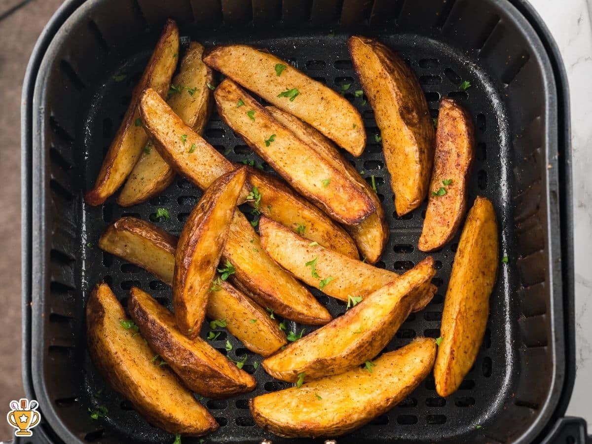 Crispy golden air fryer potato wedges cooked in a single layer in the air fryer basket and garnished with chopped parsley.