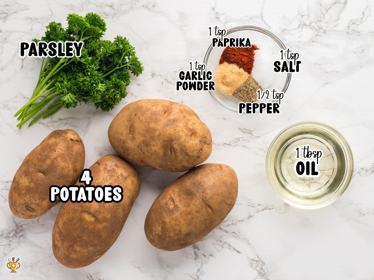 Four whole russet potatoes on a marble countertop with parsley, oil, and small bowls of paprika, garlic powder, salt, and pepper for making seasoned air fryer potato wedges.