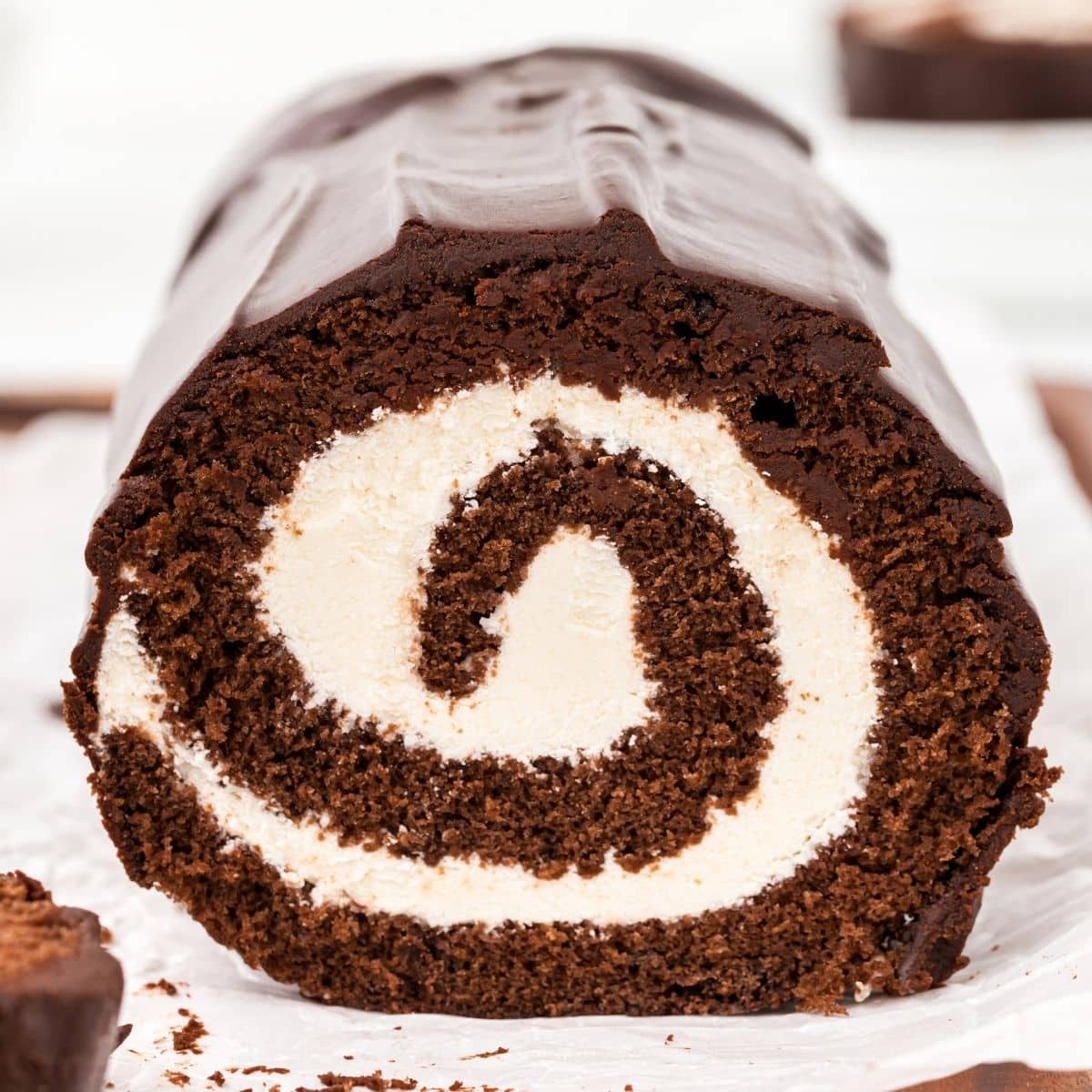 Close-up of a sliced chocolate Swiss roll cake showing a tight spiral of soft chocolate sponge and creamy ermine filling, with a smooth chocolate ganache coating on the outside.