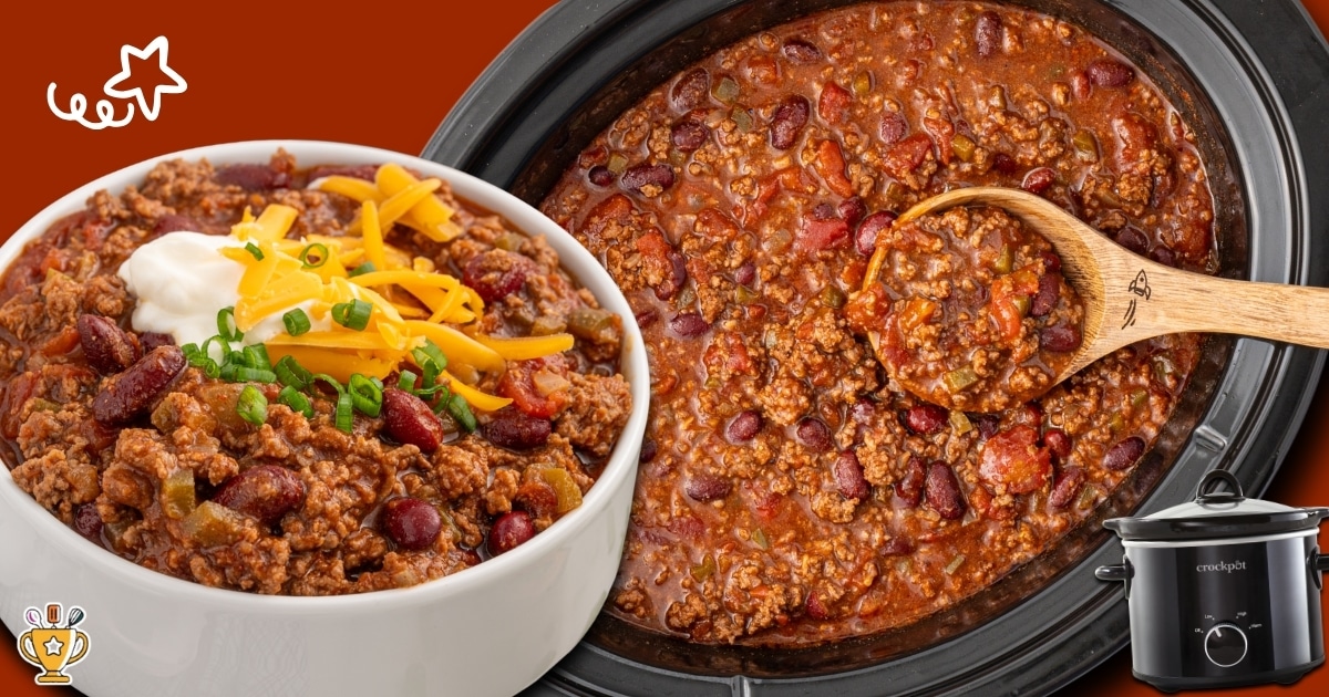 Bowl of crockpot chili topped with shredded cheese, sour cream, and green onions beside a slow cooker full of hearty beef chili.