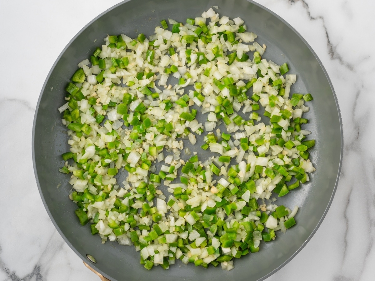 Diced onion, green bell pepper, and minced garlic cooking in a skillet to build the flavor base for crockpot chili.