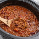 Finished crockpot chili cooking in a slow cooker with ground beef, kidney beans, tomatoes, and peppers in a thick red sauce.