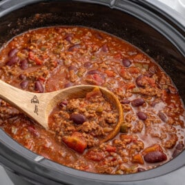 Finished crockpot chili cooking in a slow cooker with ground beef, kidney beans, tomatoes, and peppers in a thick red sauce.