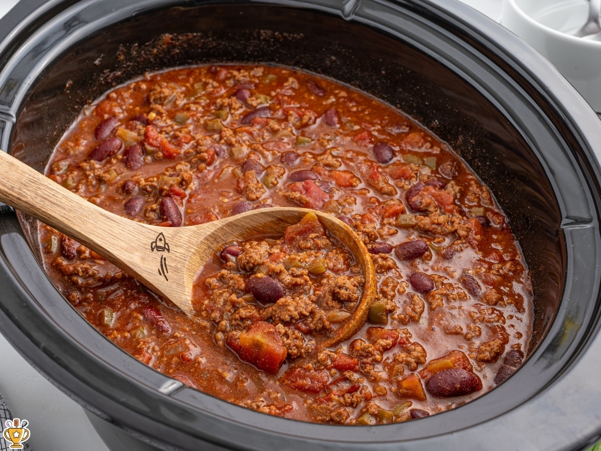 Finished crockpot chili cooking in a slow cooker with ground beef, kidney beans, tomatoes, and peppers in a thick red sauce.