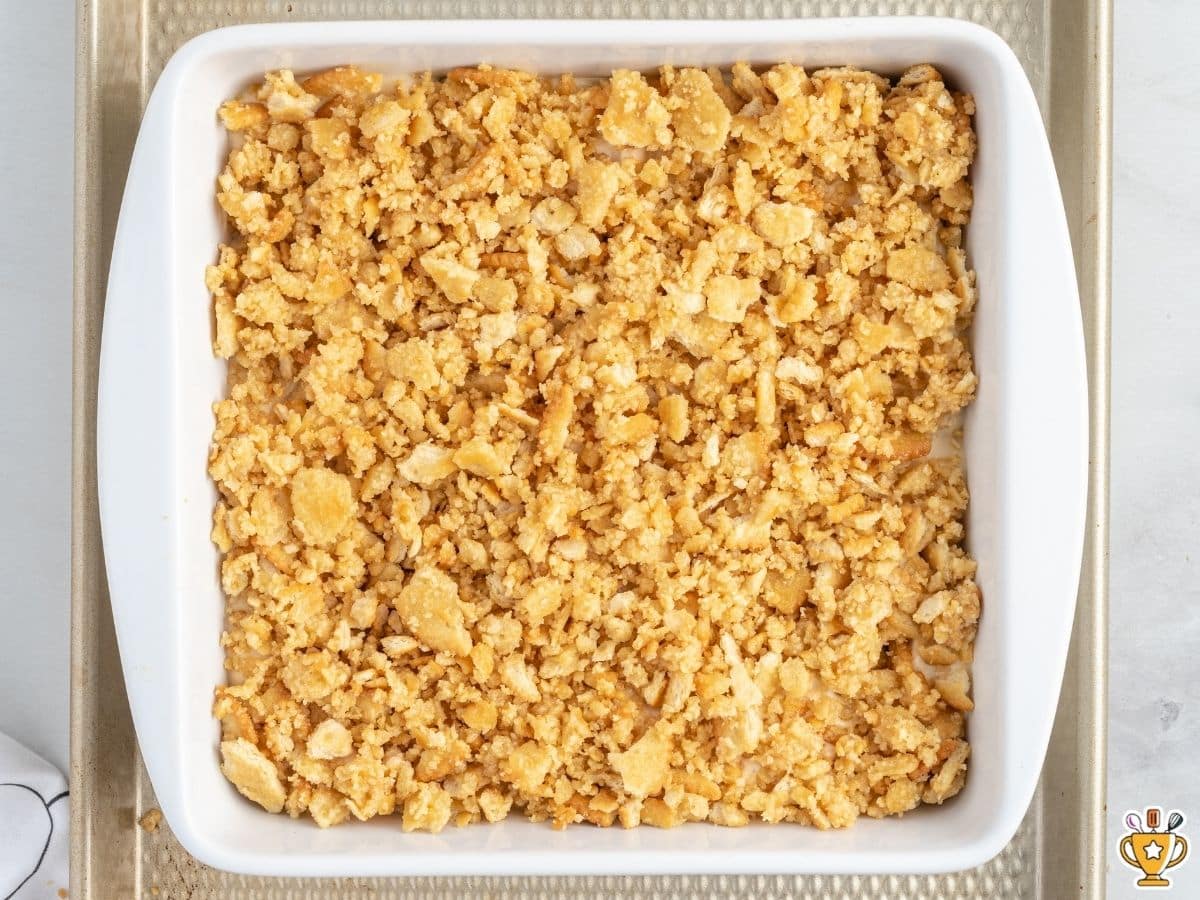 Ritz cracker chicken casserole topped with buttery crushed Ritz crackers in a white 8x8 baking dish, ready to go into the oven.