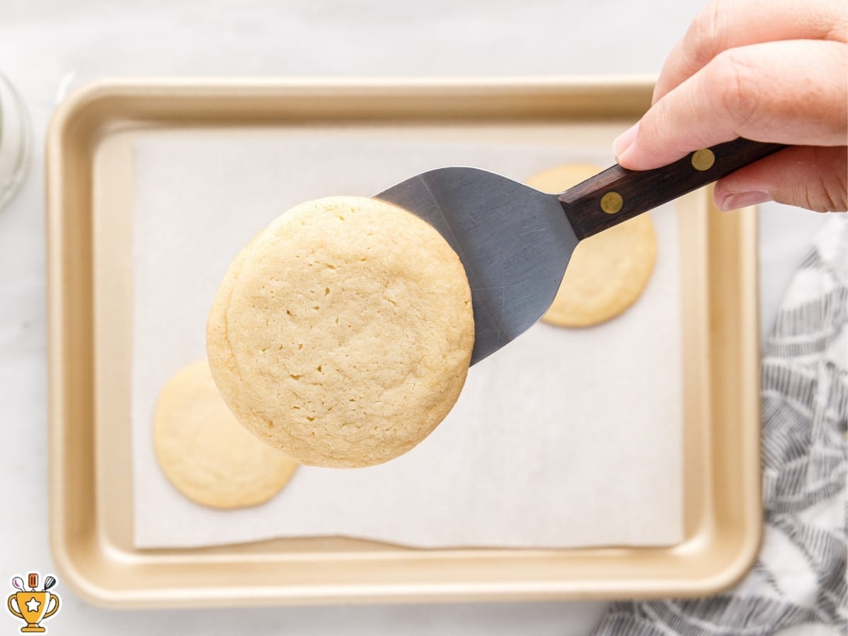 soft sugar cookie lifted from a parchment-lined baking sheet with a spatula, showing lightly golden edges and pale center