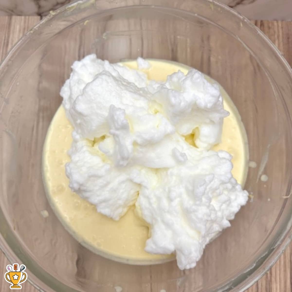 whipped egg whites set into thin lemon custard cake batter in glass bowl