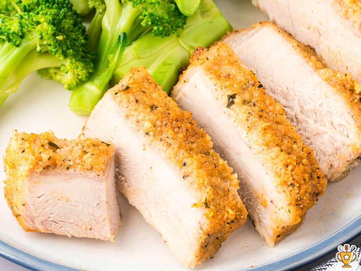 Close-up side view of thick sliced Parmesan crusted pork chops on a white plate with bright green broccoli, highlighting the crisp golden crust and tender interior.