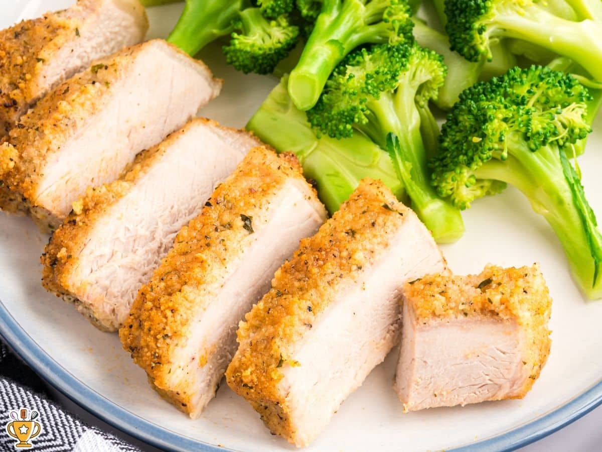 Plated Parmesan crusted pork chops sliced into thick pieces and served with steamed broccoli on a white plate, photographed from above at an angle to show the crispy coating and moist pork.