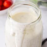Recipe card photo of homemade ranch dressing in a glass jar with a creamy drip down the side, showing specks of herbs in the dressing.