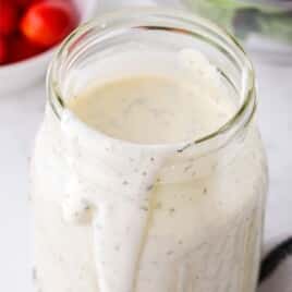 Recipe card photo of homemade ranch dressing in a glass jar with a creamy drip down the side, showing specks of herbs in the dressing.